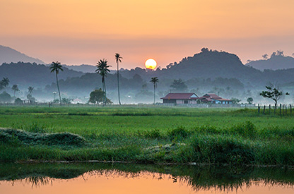 Sunset overlooking green landscape with house and hills in the background